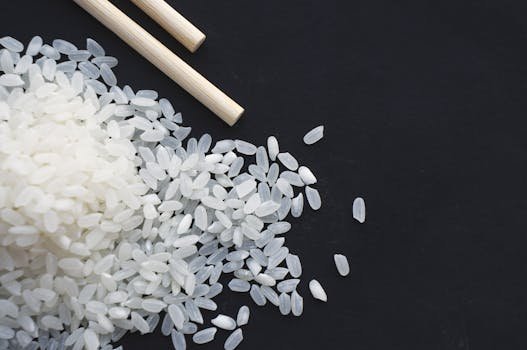 A close-up shot of raw rice grains with chopsticks on a black background, perfect for food and culinary themes.